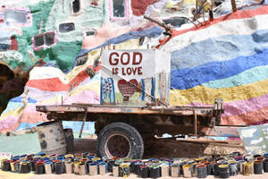 生鏽的卡車停在色彩繽紛的懸崖壁畫前，附近有「GOD IS LOVE」和油漆罐。