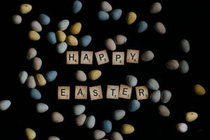 Happy Easter 用木磚拼出，黑色背景上圍繞著彩色蛋。