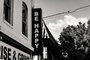 建築物上一個黑白標誌寫著「BE HAPPY」，背景有樹木和雲朵。