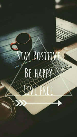 手提電腦屏幕顯示「Stay Positive Be Happy Live Free」，木桌上有咖啡杯。