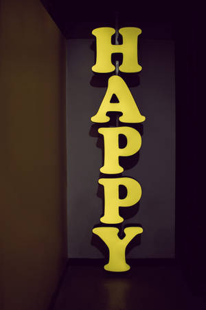 在黑暗的房間裡，一個黃色垂直霓虹燈牌拼寫著HAPPY。