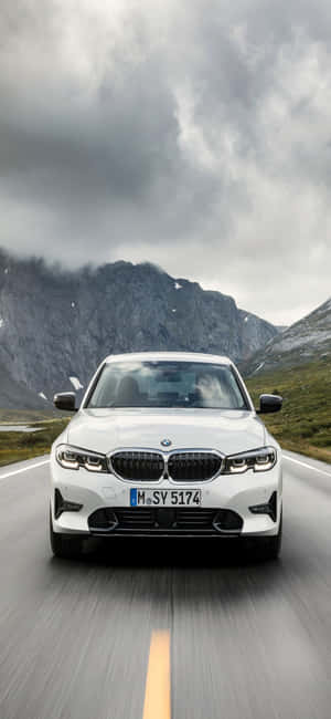 白色BMW轎車在多雲天空和岩石山峰的山路上行駛。 — Xiaomi 15 Ultra 壁紙