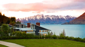 日落時分，湖邊的現代房屋，背景是白雪覆蓋的山脈。 — 湖景 壁紙