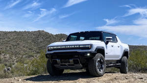 白色Hummer EV皮卡車停放在沙漠小徑上，背景有山脈和藍天。 — 汽車 壁紙