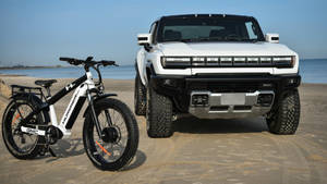 白色GMC Hummer EV SUV和電動胖胎單車停放在海邊沙灘上。 — 汽車 壁紙