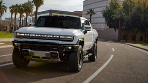 白色GMC Hummer EV電動皮卡車在日落時分行駛在棕櫚樹成蔭的城市街道上。 — 汽車 壁紙