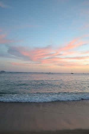 粉紅色和藍色的日落映照海洋，帆船和溫柔的海浪在沙灘上