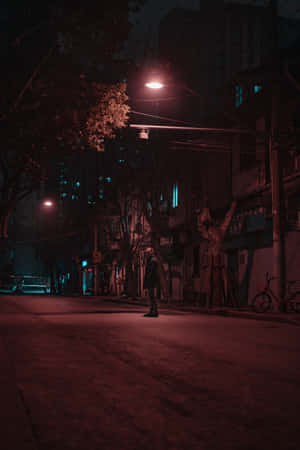 一個孤獨的人夜晚站在昏暗的城市街道上，在一盞紅色街燈下。
