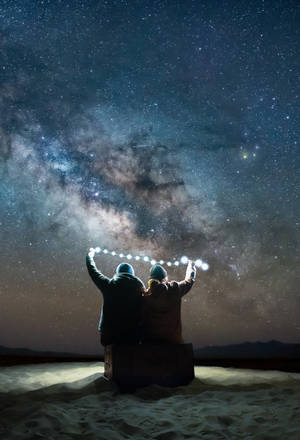 兩個人在沙漠中星空下舉著燈光。