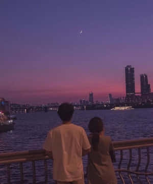 兩個人在暮色中觀看城市天際線上的月亮。 — 情侶 GIF 壁紙