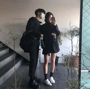 一對穿著黑色服裝的情侶在樓梯和植物附近的室內拍攝鏡子自拍照。 — 情侶 GIF 壁紙