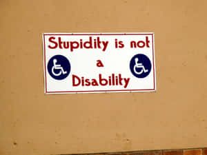 一個諷刺標牌，寫著「Stupidity is not a Disability」，帶有輪椅圖標。