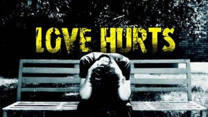 坐在長椅上，在 'LOVE HURTS' 字樣下低着頭的人。