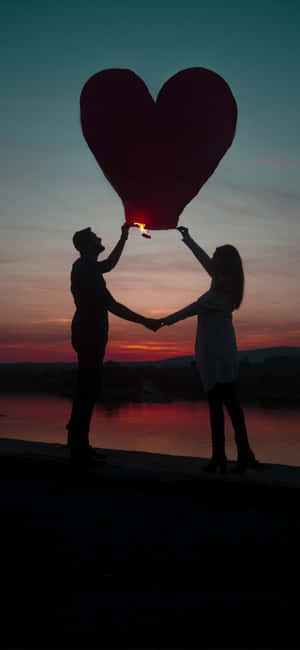 一對情侶在日落時分在湖上釋放一個愛心形狀燈籠。 — 情侶 GIF 壁紙