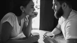 一對情侶在寧靜的咖啡館裡，在柔和燈光下喝咖啡，進行親密的眼神交流。