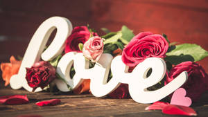 白色 'love' 字母被紅粉玫瑰環繞在木頭上。