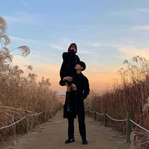 一對情侶在夕陽下穿著黑色外套在高高的蘆葦中擁抱。 — 浪漫愛情 壁紙