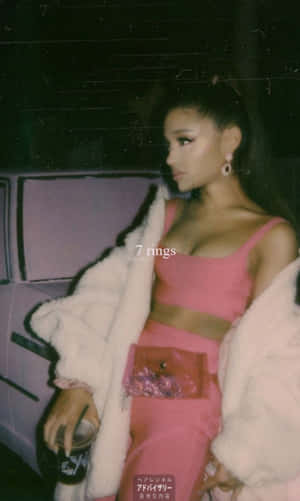 Ariana Grande 身穿粉紅色服裝和白色毛皮大衣，在夜間站在汽車旁。