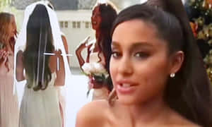 Ariana Grande 在婚禮上對著鏡頭微笑，背景有伴娘。