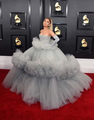 Ariana Grande 身穿灰色薄紗長裙企喺紅地毯上，身後有格林美獎座。