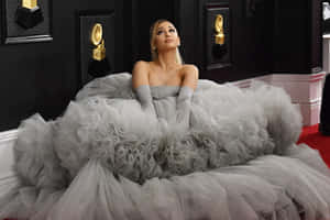 Ariana Grande 身穿灰色薄紗禮服，在紅地毯上擺姿勢，背景有格林美獎項。
