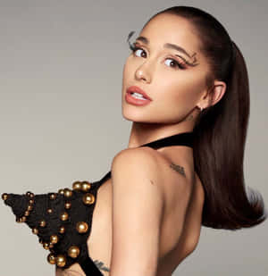 Ariana Grande 身穿黑色珠飾上衣，帶有金色點綴，搭配戲劇性的睫毛。