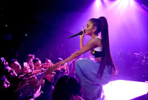 歌手 Ariana Grande 在舞台上表演，粉絲伸手觸摸她。