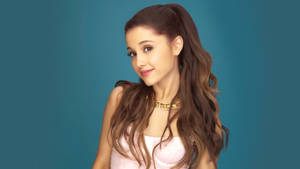Ariana Grande 身穿粉紅色上衣和金色頸鏈，背景為青色。