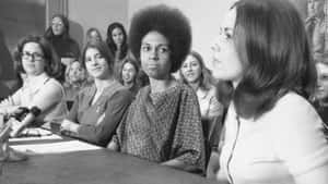 1970年代記者會上使用麥克風的女性。
