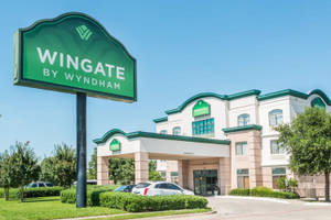 陽光明媚的日子裡，帶有綠色標誌和停放汽車的Wingate by Wyndham酒店。
