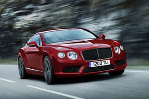 紅色 Bentley Continental GT 在模糊背景的山路上疾馳。