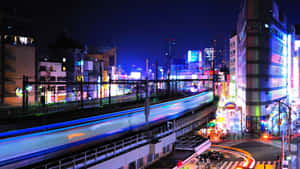 霓虹燈照亮都市夜景，火車光軌和發光廣告牌。 — iMac 壁紙
