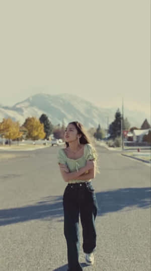年輕女性站在寧靜的街道上，身後有山脈和秋天的樹木。