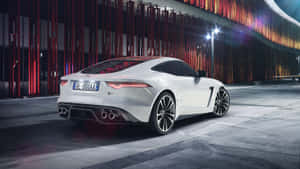 白色Jaguar F-Type跑車夜間停放在霓虹燈下，靠近現代建築。 — 2560x1440 壁紙