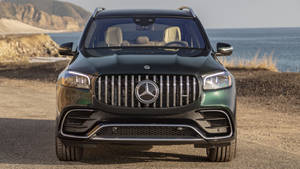 一架綠色平治 GLS SUV 停泊喺沿海泥路嘅正面視圖。