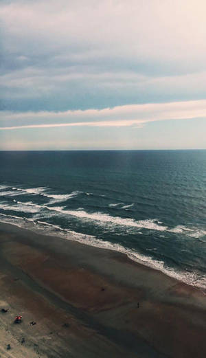鳥瞰海洋波浪在沙灘上拍打，天空多雲。
