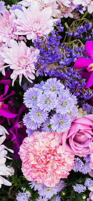 一束密集的粉紅蜜桃玫瑰、康乃馨和紫色花朵。