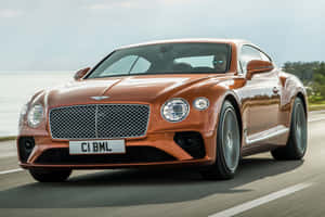 橙色 Bentley Continental GT 在靠近海洋的海岸公路上行駛。