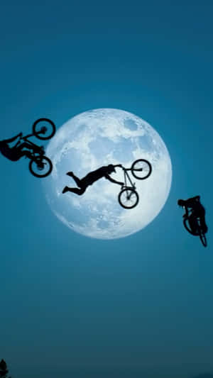 三名BMX車手在夜間對著滿月表演空中特技。
