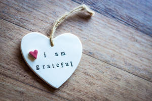 白色陶瓷心形裝飾品，上面有「i am grateful」字樣，放置在木質表面上。