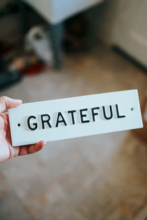 手拿著一個白色標牌，上面用黑色字母寫著grateful。 — Huawei MatePad Air (2025) 壁紙