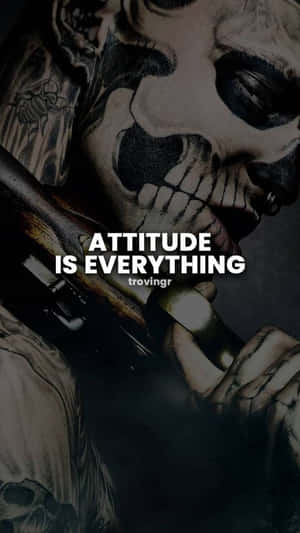 一個有紋身、骷髏臉的人手持槍支，上面有粗體文字寫著「attitude is everything」。 — 語錄 壁紙