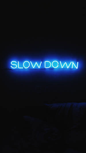 在黑暗臥室中寫著 slow down 的藍色霓虹燈牌。
