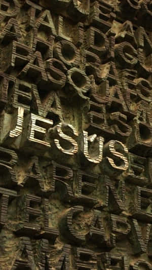 雕刻石牆，凸起字母拼出JESUS，以金色照亮。