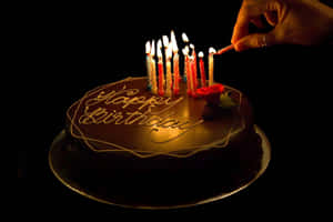 手吹熄巧克力蛋糕上的生日蠟燭，蛋糕上有'Happy Birthday'糖霜。