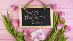 粉紅色鬱金香和禮物盒圍繞著一塊帶有「Happy Mother's Day」訊息的黑板。