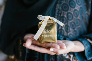 雙手展示一個帶有白色絲帶的金色Eid Mubarak禮物盒。