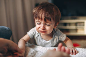 一個幼兒在地毯上哭著伸手去抓大人的手。