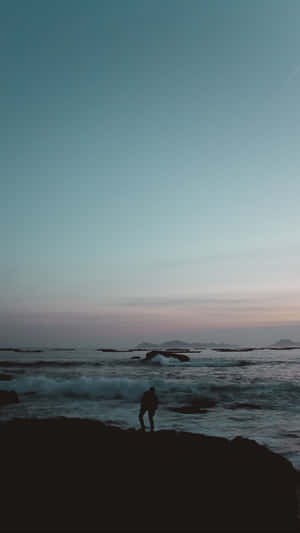 人站在岩石上觀看黃昏的海浪