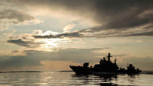 金色日落和戲劇性雲層中，軍艦在水上航行的剪影。